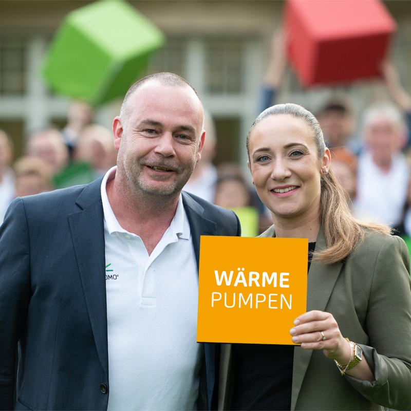 Zwei Personen halten ein Schild mit der Aufschrift „Wärmepumpen“ bei einer Veranstaltung.
